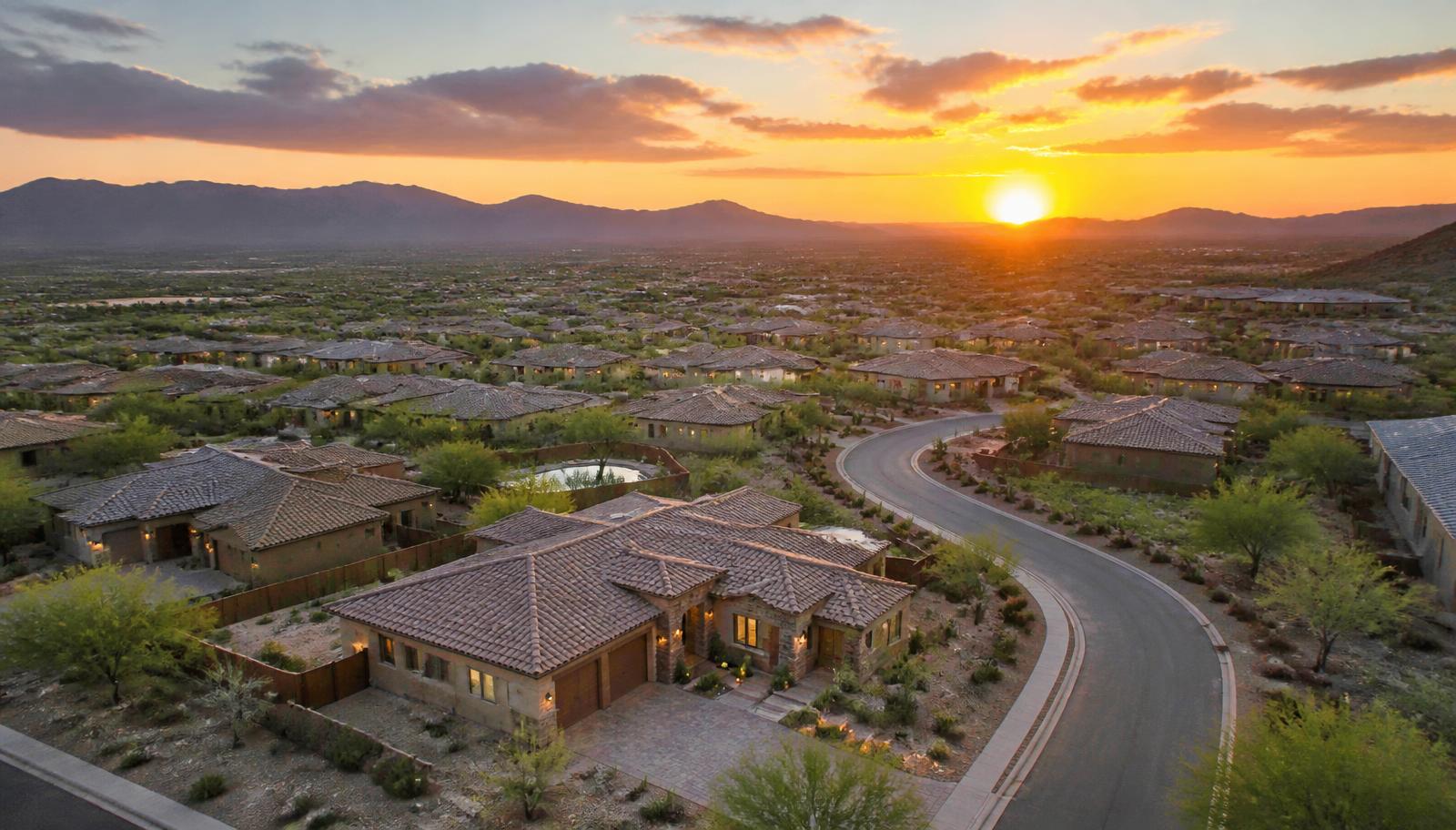 Aerial view of an Arizona desert community at sunset with new homes and mountains on the horizon